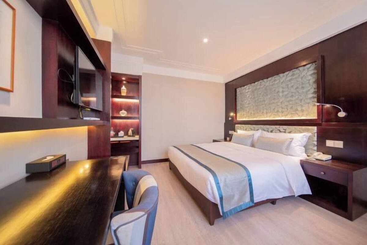 Een hotelkamer met een bed, nachtkastje, stoel, bureau en ingebouwde planken.