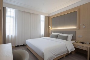 A modern hotel room with a large bed, a bedside table with a lamp, a desk, and a large window with curtains. - Kunlun Hotel (Nantong)