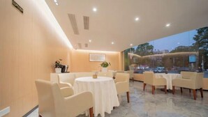 A modern hotel lobby with a marble floor, round tables with white tablecloths, and beige chairs. - Kunlun Hotel (Nantong)