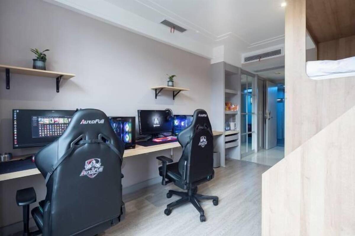 Een modern kantoor met twee gaming stoelen, een bureau met meerdere monitoren en een boekenkast met planten.