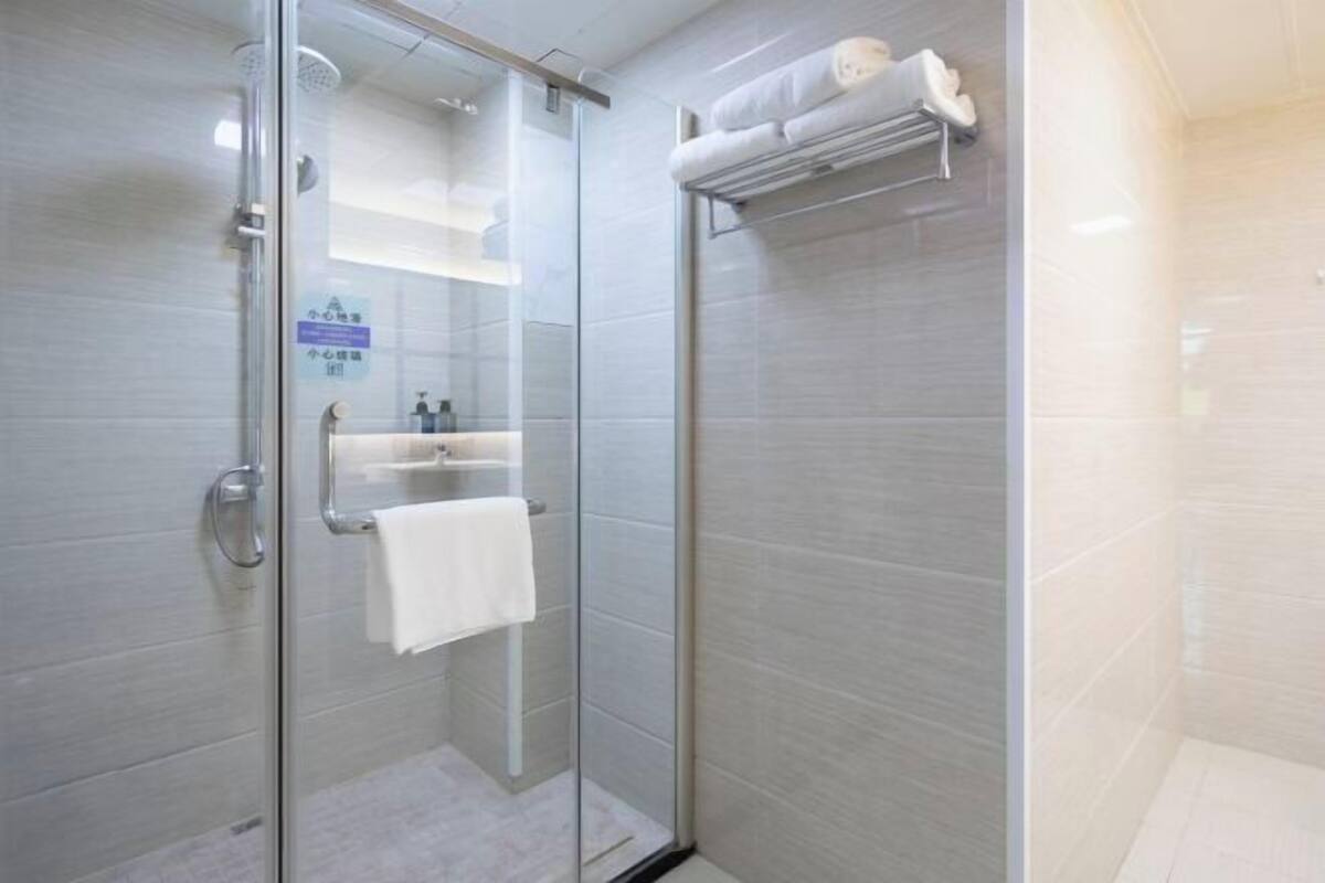 A modern shower with glass doors, a white towel, and a shelf with toiletries.
