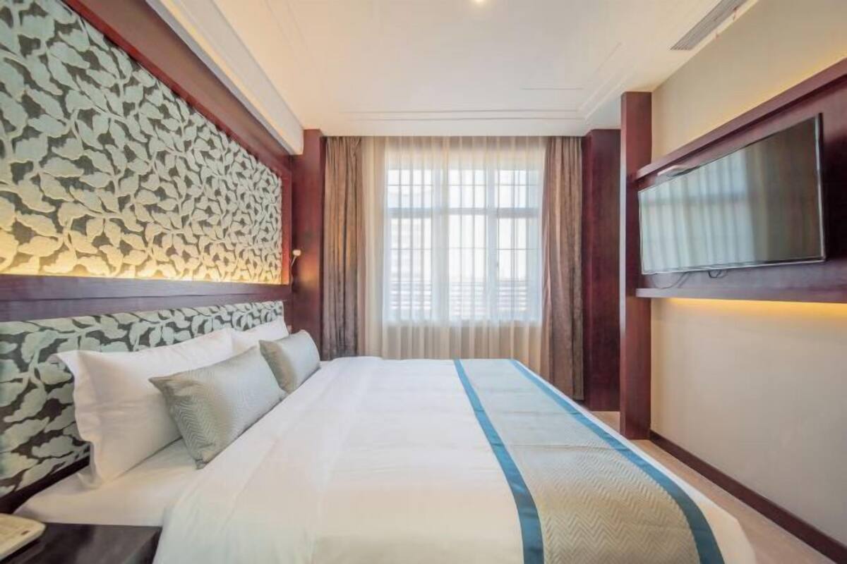 Een hotelkamer met een bed, een televisie, een raam met gordijnen en een behang met een patroon.