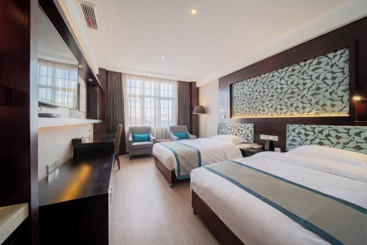 Een hotelkamer met twee bedden, een bureau, een stoel, een groot raam en een decoratief wandpaneel.