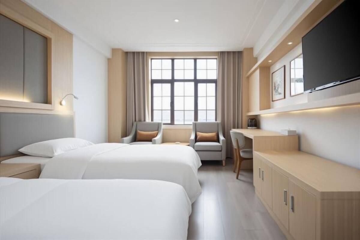 Een hotelkamer met twee bedden, een bureau, een stoel en een groot raam.