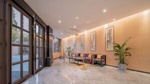 A spacious lobby with a marble floor, a seating area with a sofa and chairs, and large windows on the left side. - Kunlun Hotel (Nantong)