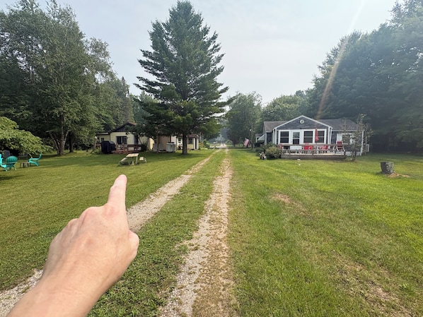 A grassy pathway leading to a house with a porch and outdoor seating. - Michele’s Landing, Charming cottage in amazing Lake Leelanau, on narrows w/ dock (Lake Leelanau)
