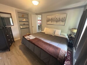 A bedroom with a bed, a dresser, a television, a painting, and a lamp. - Michele’s Landing, Charming cottage in amazing Lake Leelanau, on narrows w/ dock (Lake Leelanau)