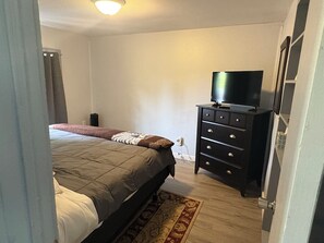 Un dormitorio con cama, cómoda, televisión y estante en la pared.