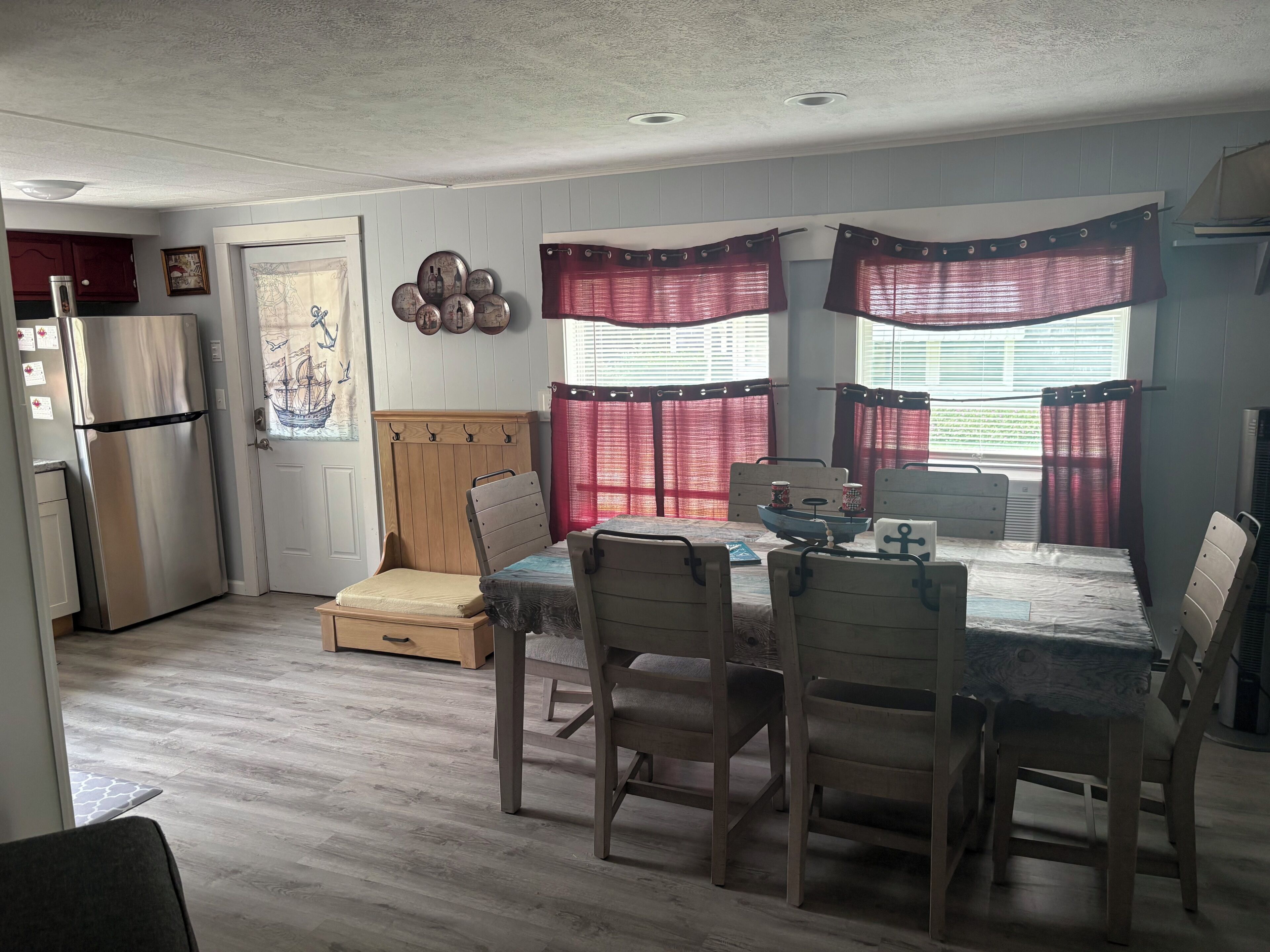 Un espacio habitable compacto con kitchenette, una zona de comedor con mesa y sillas, y una cama con cabecera.