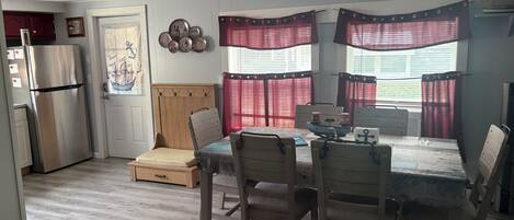 Un espacio habitable compacto con kitchenette, una zona de comedor con mesa y sillas, y una cama con cabecera.