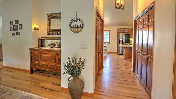 A spacious hallway with wooden flooring, a wooden dresser, a vase with greenery, and a kitchen area with wooden cabinets and a refrigerator.