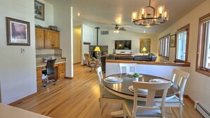 A spacious kitchen with wooden cabinets, a dining area with a round table and white chairs, and a living area with a sofa and a TV.