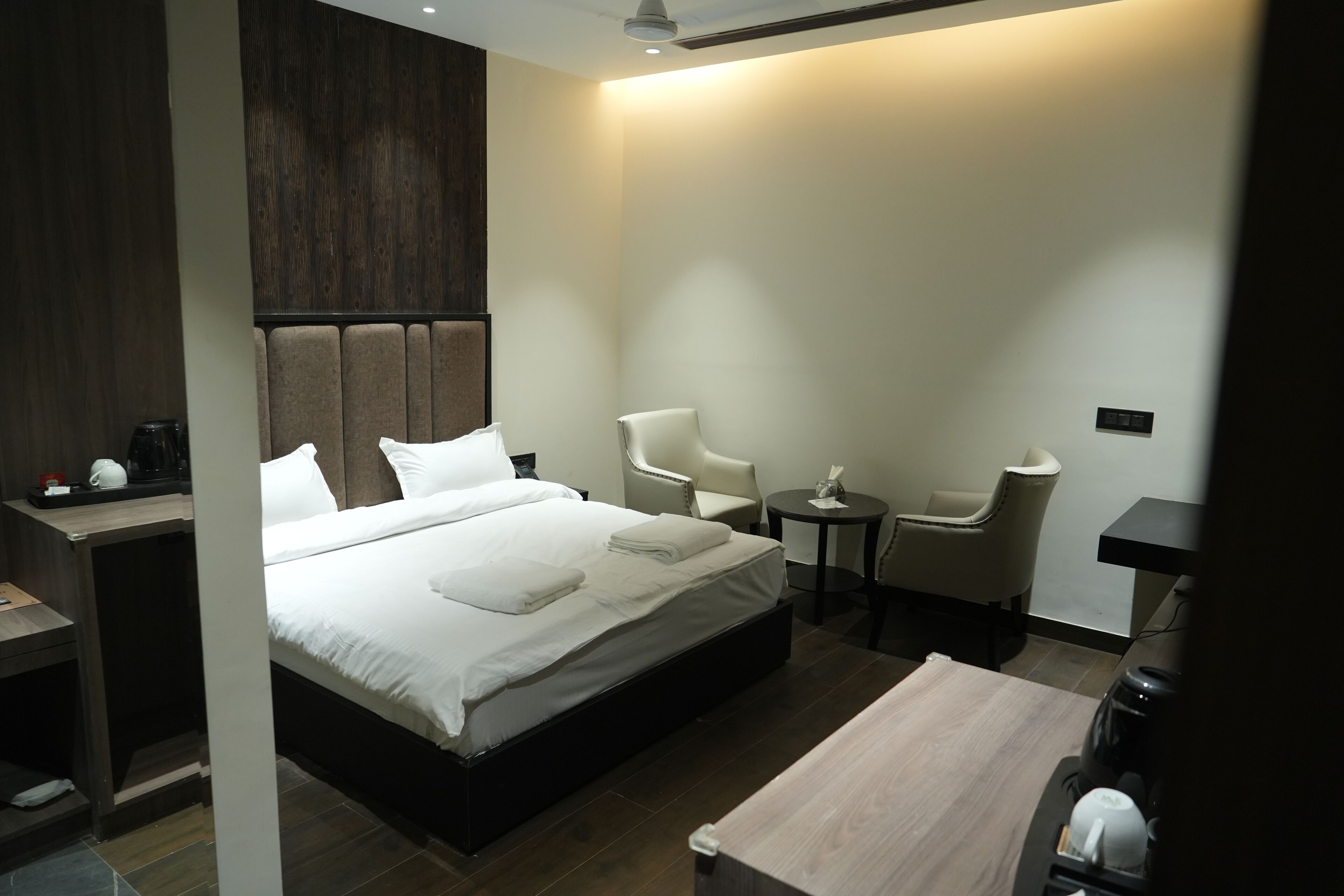A modern hotel room with a large bed, two chairs, a small table, and a coffee machine.