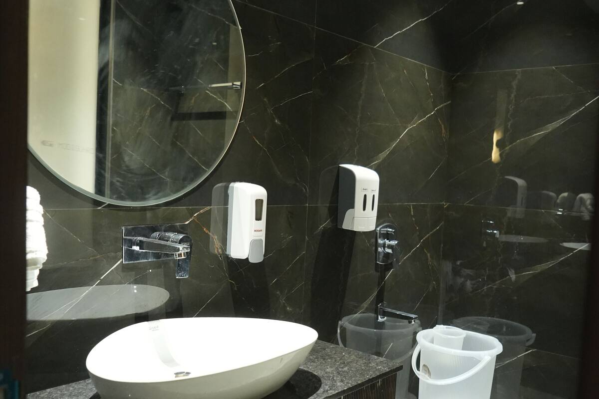 A modern bathroom with a large oval sink, a round mirror, and a handheld soap dispenser.