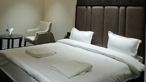A hotel room with a large bed, a headboard, a chair, and a small table with a bottle and tissues.