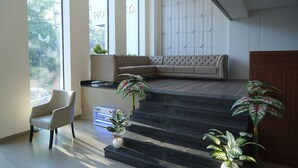 A modern interior with a sofa, a chair, and a staircase with potted plants.