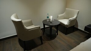 A small, private room with two white leather chairs and a round table, featuring a bottle of water and a glass.
