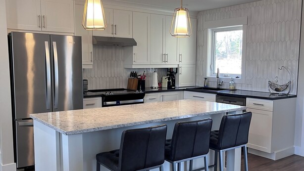 A modern kitchen with white cabinetry, stainless steel appliances, and a central island with bar stools.