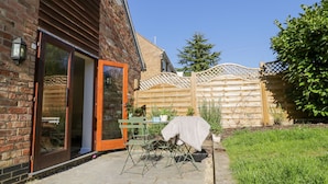 A patio with a table and chairs, a covered grill, and a wooden fence. - Little Barn (Stratford-upon-Avon)