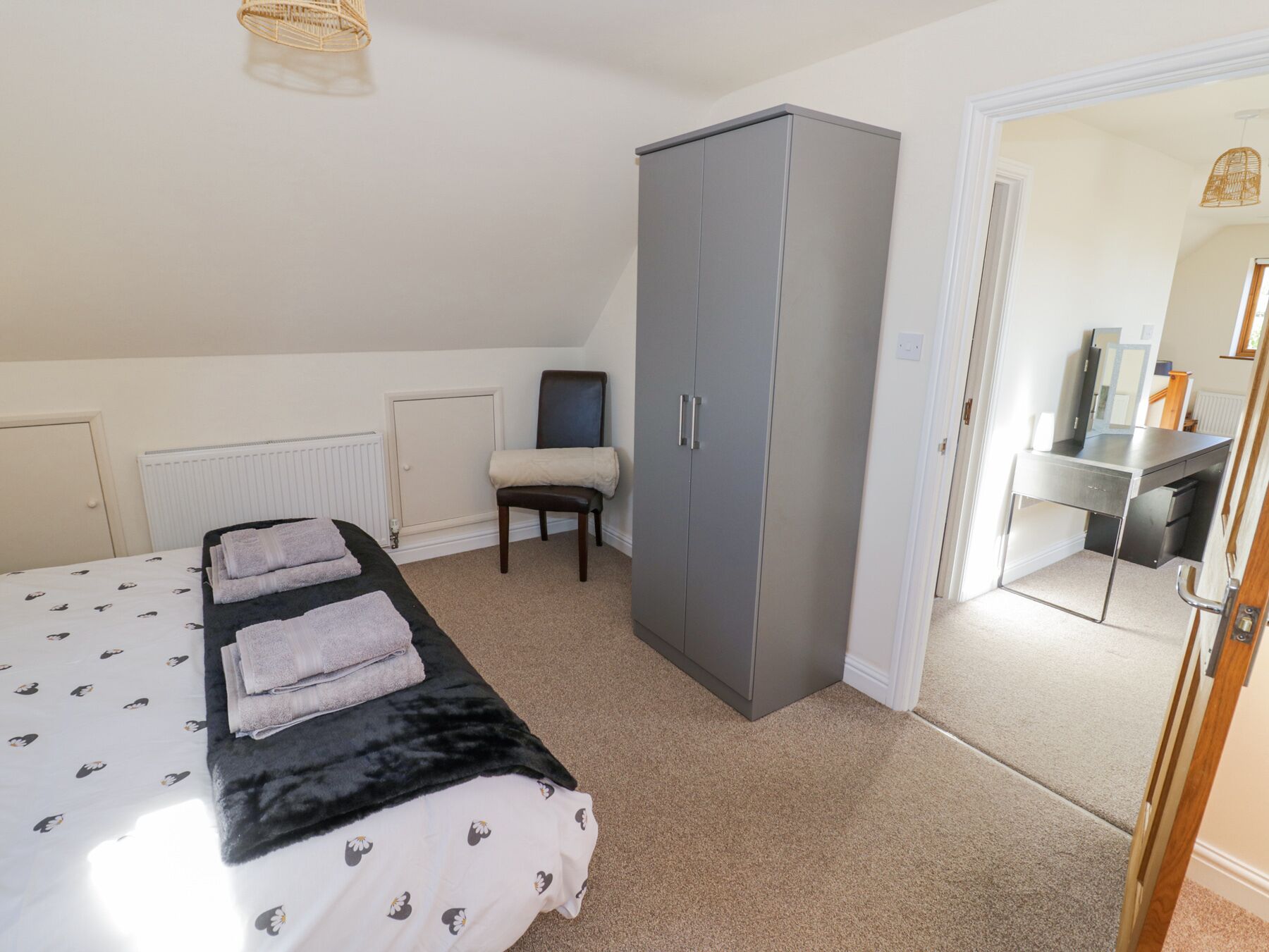 Ein Schlafzimmer mit einem Bett, einem grauen Kleiderschrank, einem Sessel und einem Schreibtisch mit Spiegel.