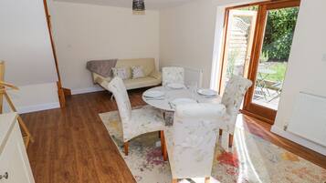 A dining area with a table set for four, surrounded by floral-patterned chairs, a sofa, and a radiator.
