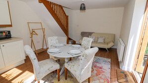 A cozy living room with a round dining table, floral chairs, a sofa, and a wooden staircase. - Little Barn (Stratford-upon-Avon)