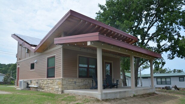 Une maison à deux étages dotée d’un porche abrité, de fondations en pierre et d’un panneau solaire sur le toit.
