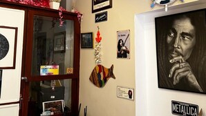 A room with a large window, a blue chair, a table with a vase, and various wall decorations including a clock, a framed portrait, and a ship's wheel. - Ada İnan Pansiyon (Adalar)