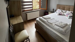 A bedroom with a bed, a desk, a chair, a radiator, and a window with blinds. - Ada İnan Pansiyon (Adalar)