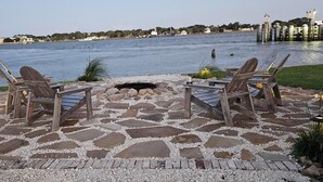 Un patio con baldosas de piedra, dos sillas de madera y un pozo para fuego.