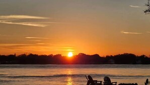 A sunset over a body of water with chairs on the shore. - The Riverhouse (Jacksonville)