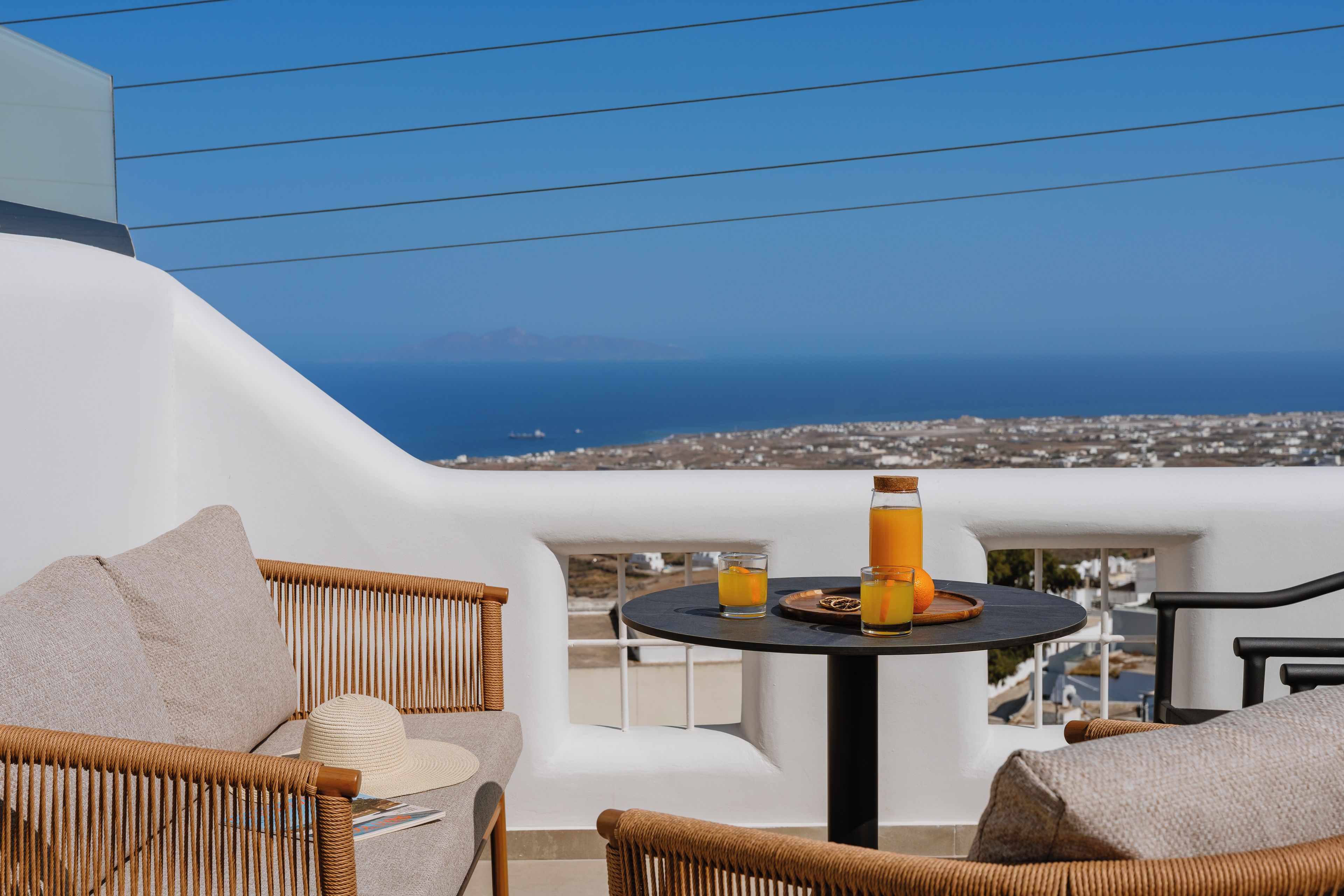 Un balcon agrémenté de meubles en osier, une table avec des boissons et une vue sur la mer et les bâtiments.