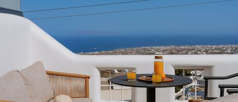 Un balcon agrémenté de meubles en osier, une table avec des boissons et une vue sur la mer et les bâtiments.