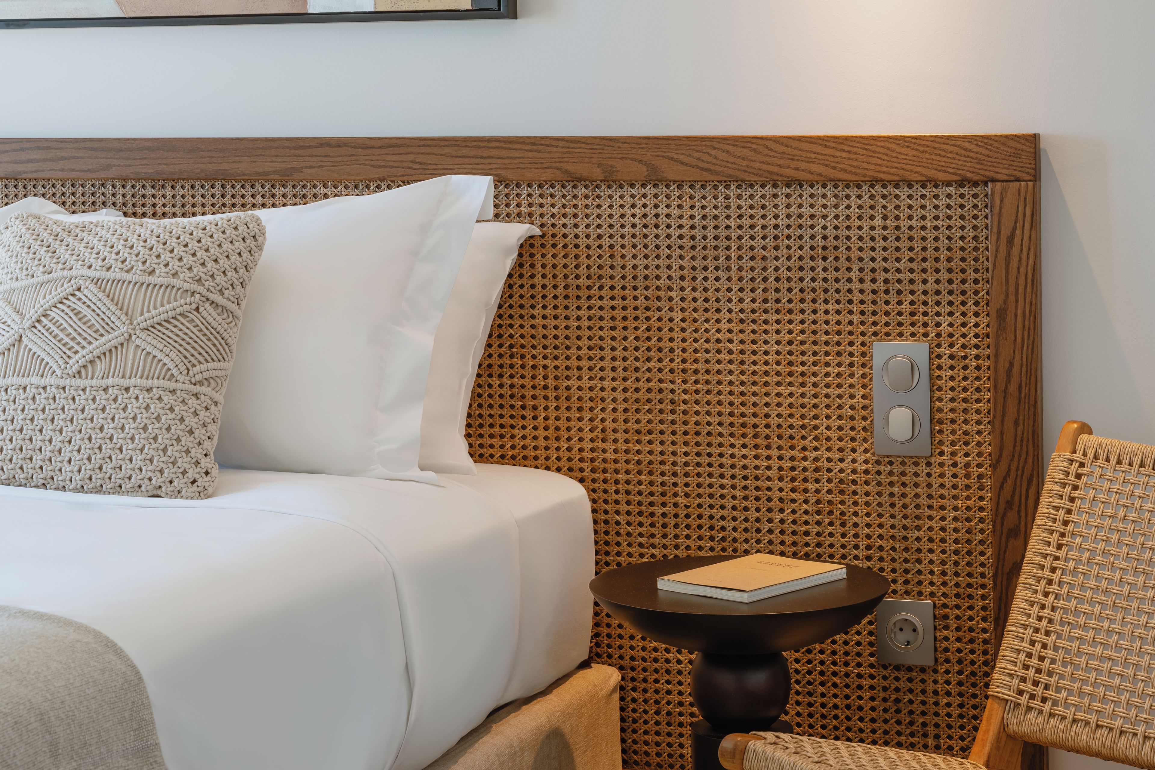 Una habitación de hotel con una cama, una mesita de noche con un libro y un cabecero tejido.