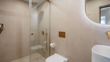 A bathroom with a glass-enclosed shower, a toilet, and a sink.
