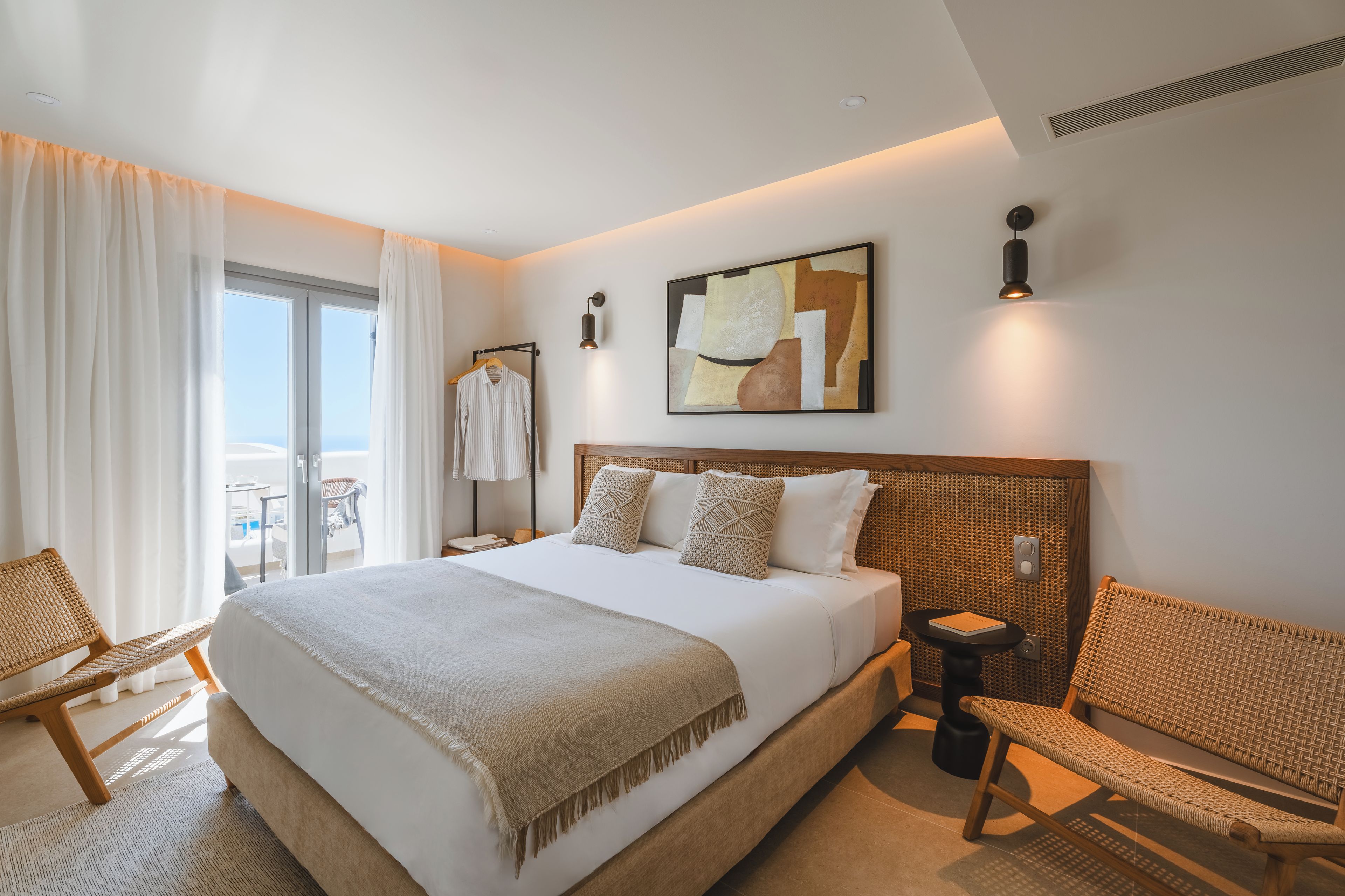 A hotel room with a large bed, a view of the outdoors, a seating area, and a small table with a book.