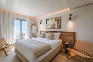 A hotel room with a large bed, a view of the outdoors, a seating area, and a small table with a book. - Breaq Santorini - Margarita Hotel (Santorini)