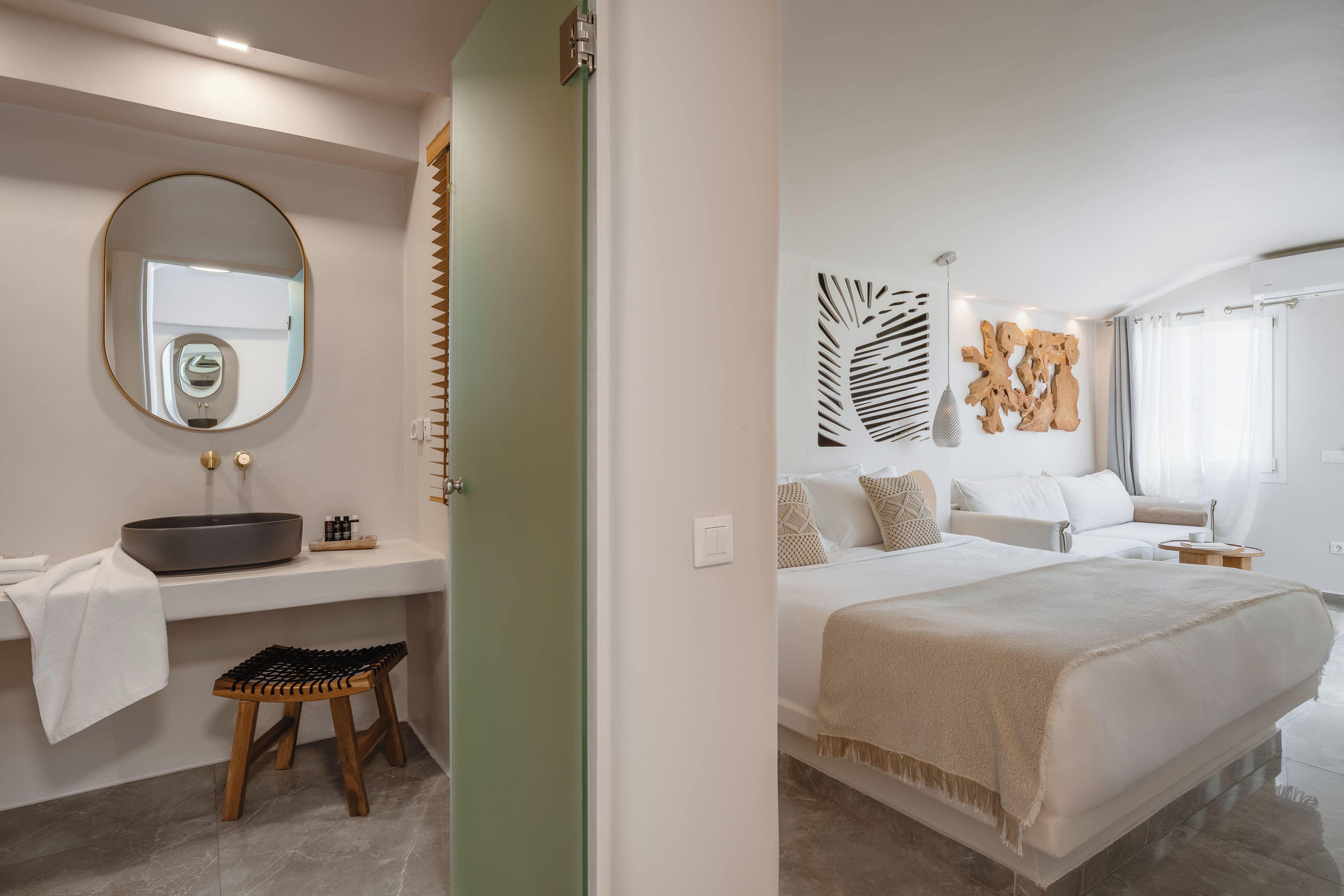 Ein modernes Schlafzimmer mit einem großen Bett, einem Nachttisch, einem Wandspiegel und einem Badezimmer mit Waschbecken und Handtuchhalter.