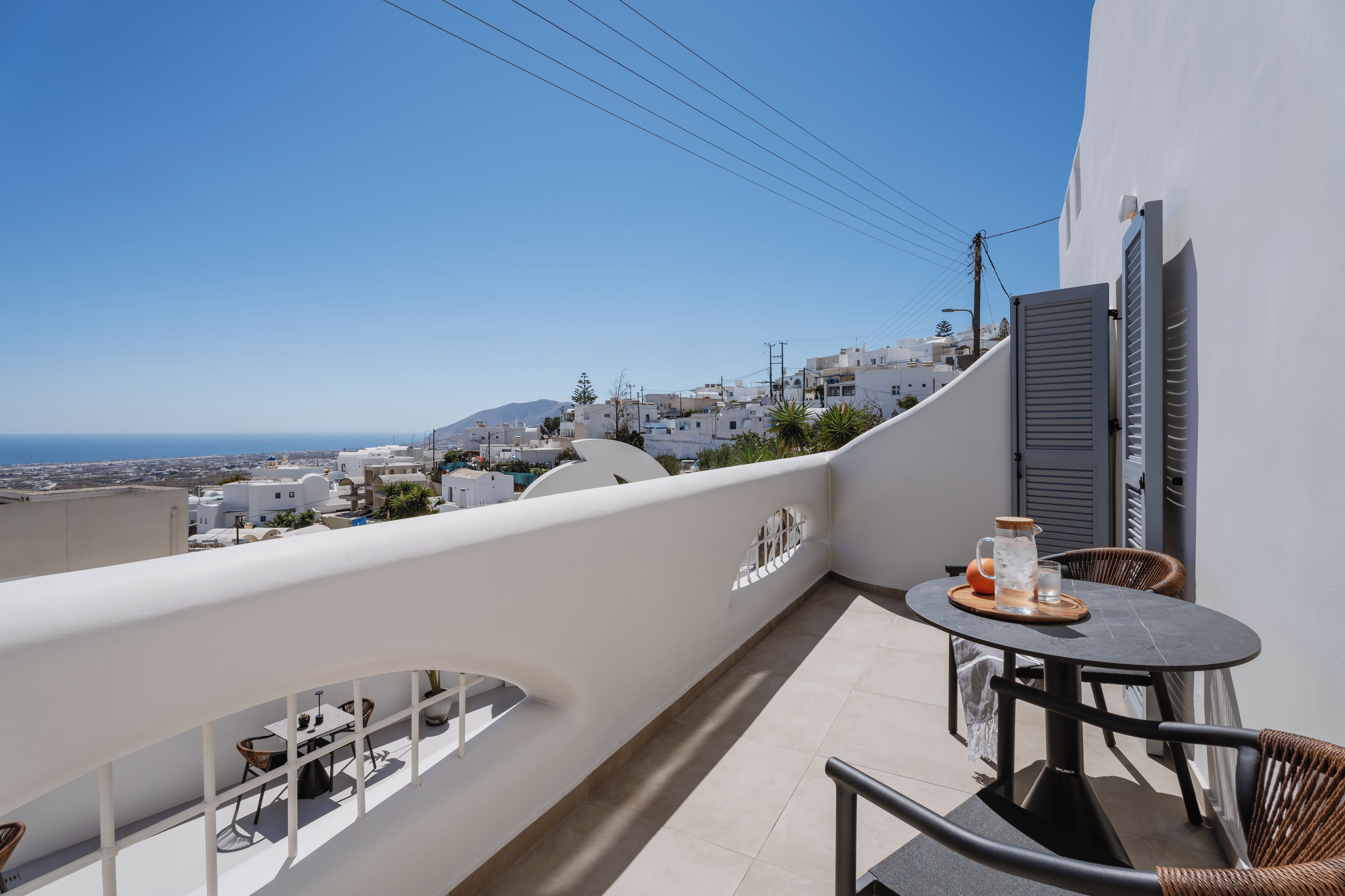 Een balkon met een tafel en stoelen, met uitzicht op een kustplaatsje met witte gebouwen en een heldere lucht.
