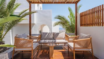 An outdoor seating area with wicker furniture and a wooden table, surrounded by white walls and palm trees.