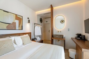 Een hotelkamer met een bed, een nachtkastje met een lamp, een spiegel, een houten bureau met een koffiezetapparaat, en een badkamer zichtbaar door een geopende deur.