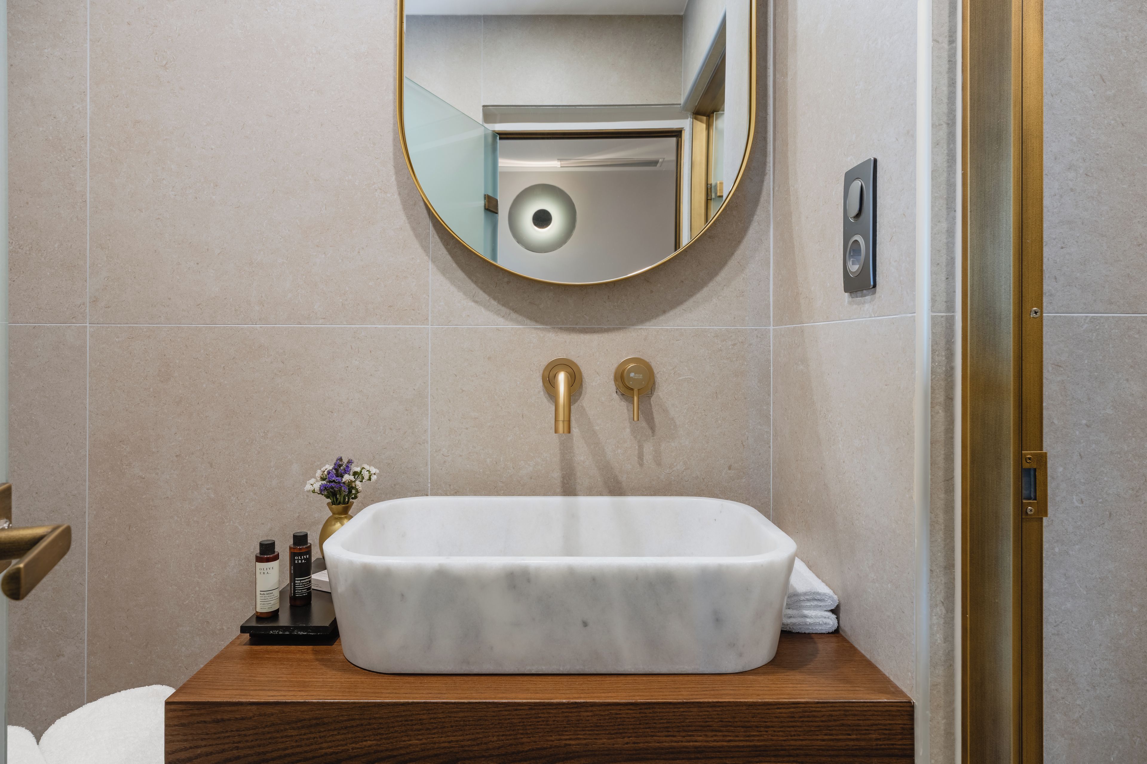 Une salle de bain avec un lavabo en marbre blanc, des robinets dorés et un miroir rond.