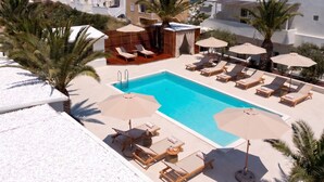 A rooftop pool area with lounge chairs and umbrellas, surrounded by palm trees and a view of the sea. - Breaq Santorini - Margarita Hotel (Santorini)