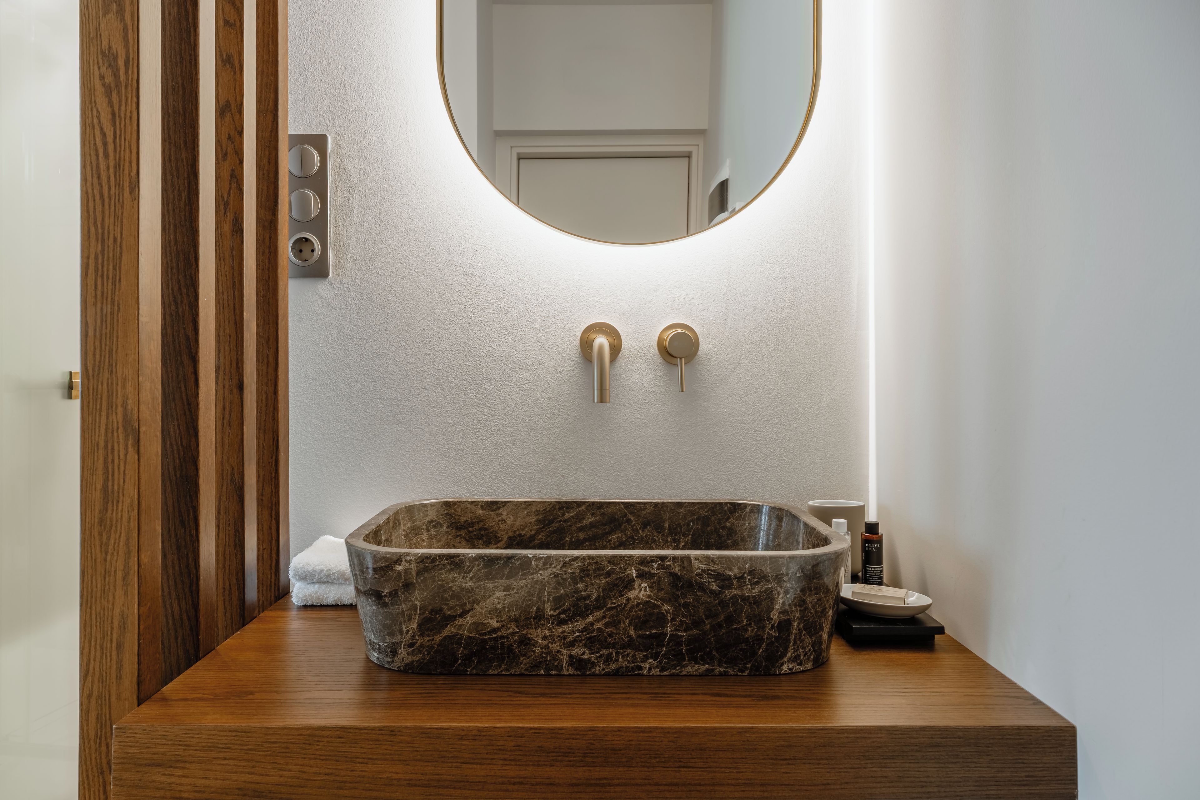 Un baño con lavamanos de mármol, tocador de madera y espejo montado en la pared.