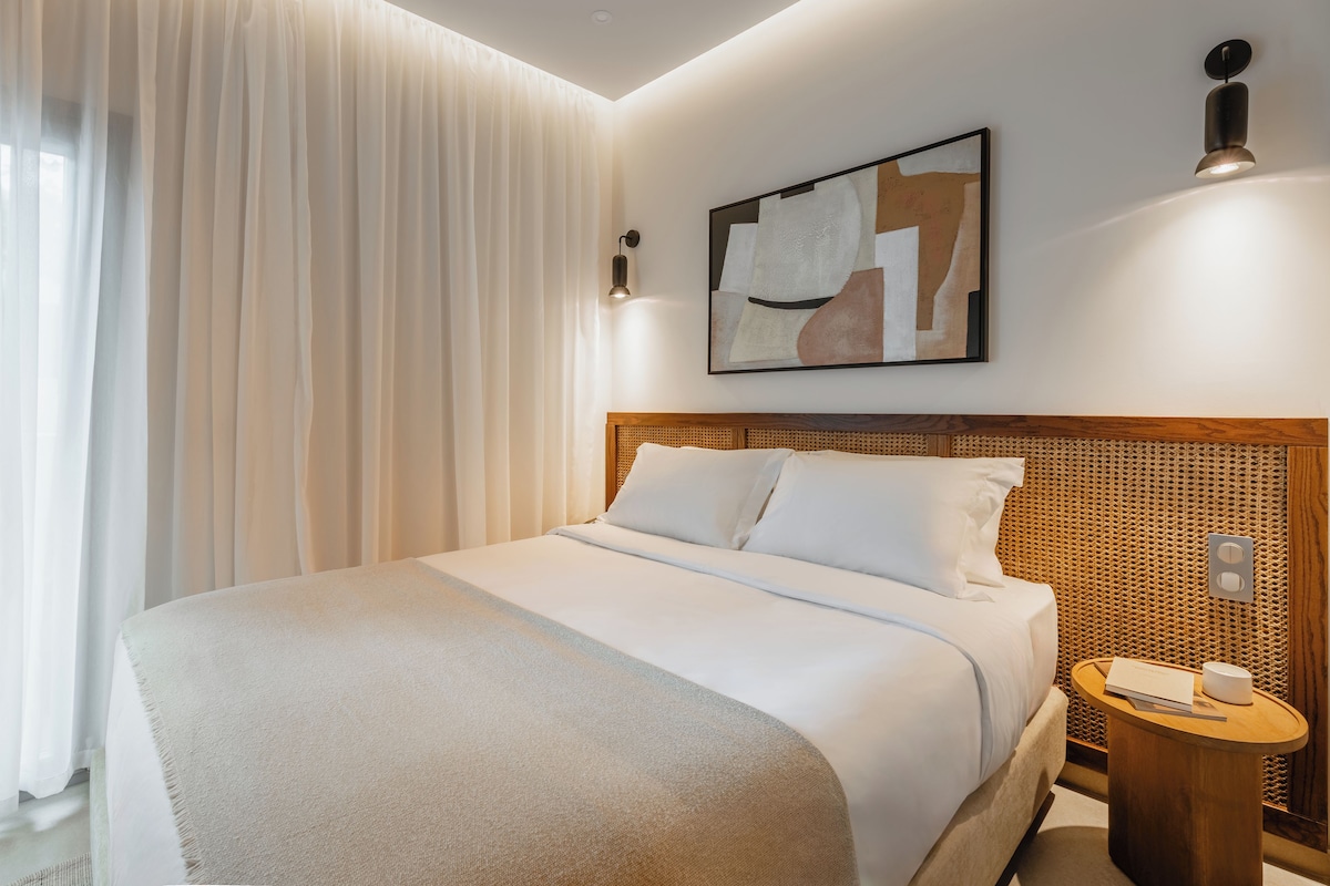 Una habitación de hotel con una cama, una mesita de noche, una lámpara de pared y un cuadro.