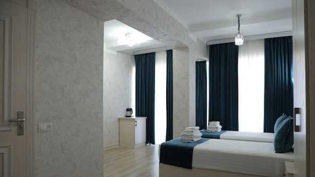 A hotel room with a bed, a bedside table, a lamp, and a view of the outdoors. - HOTEL MERCURI MERIDIAN (Bukhara)