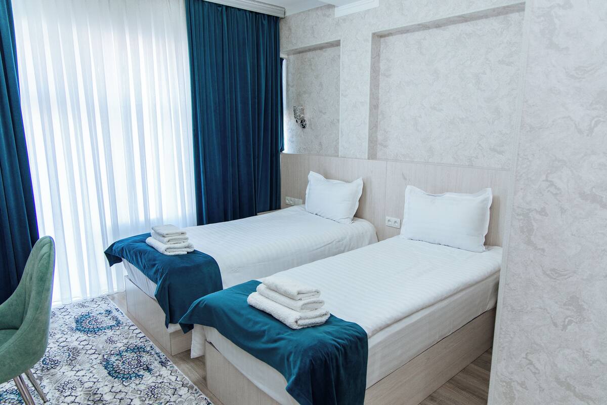 A hotel room with two beds, a green chair, and a patterned rug.