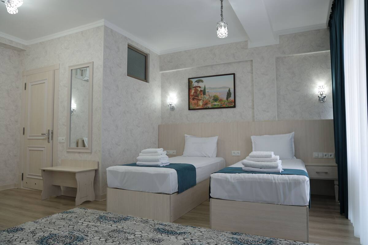 A hotel room with two beds, a desk, a mirror, and a painting on the wall.