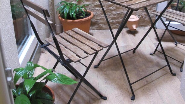 A small outdoor seating area with a table and chairs, a potted plant, and a textured wall. - Apartment in La Alameda de Hércules (Sevilla)