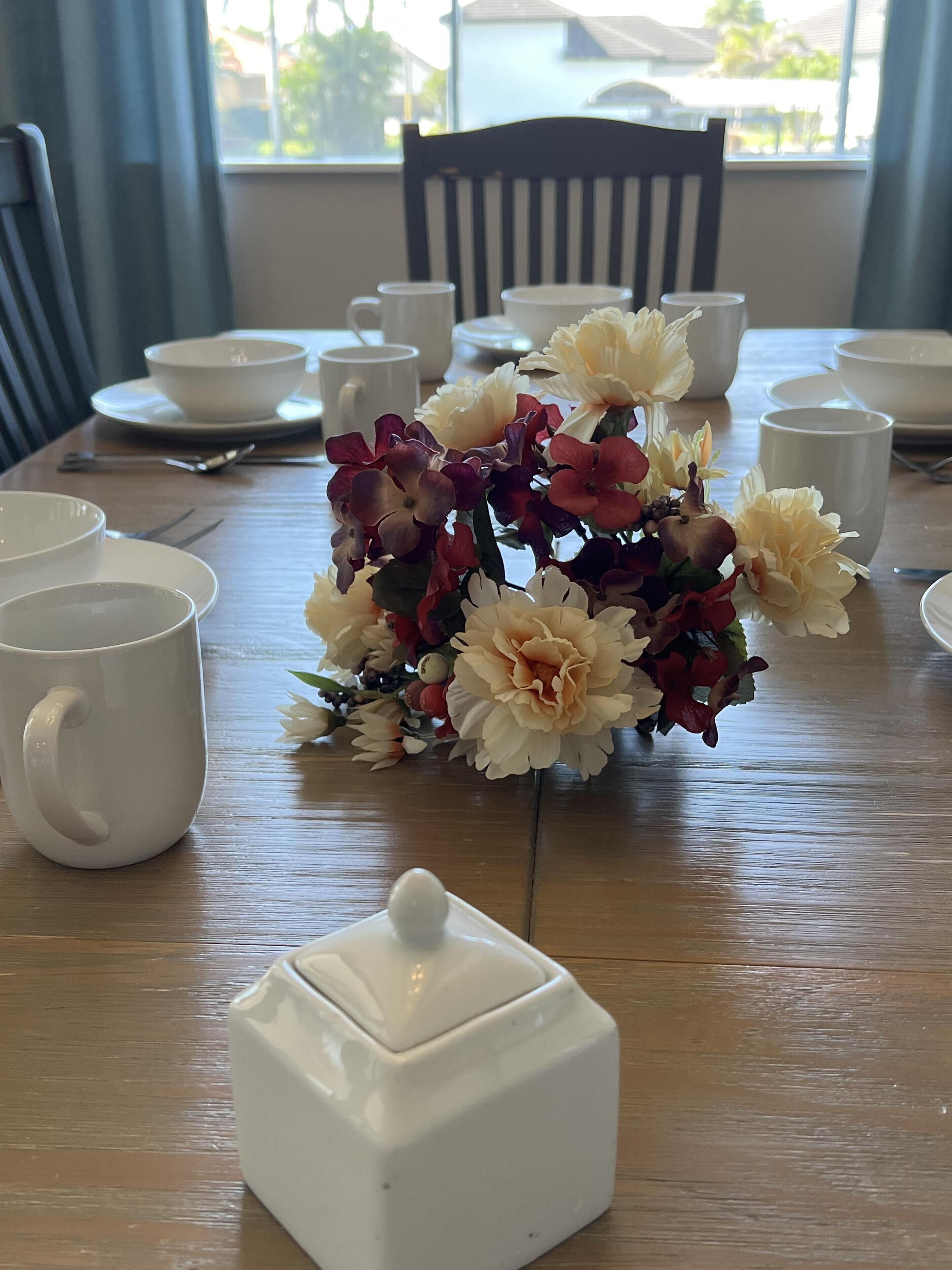 A dining table with white cups, saucers, and a white teapot.